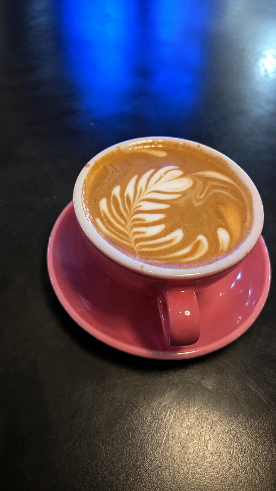 Flat white with rosetta latte art in a pink cup and saucer on a dark counter